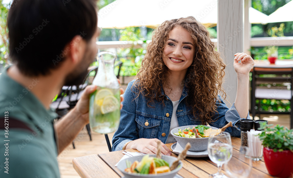 Happy couple sitting outdoors on terrace restaurant, talking.