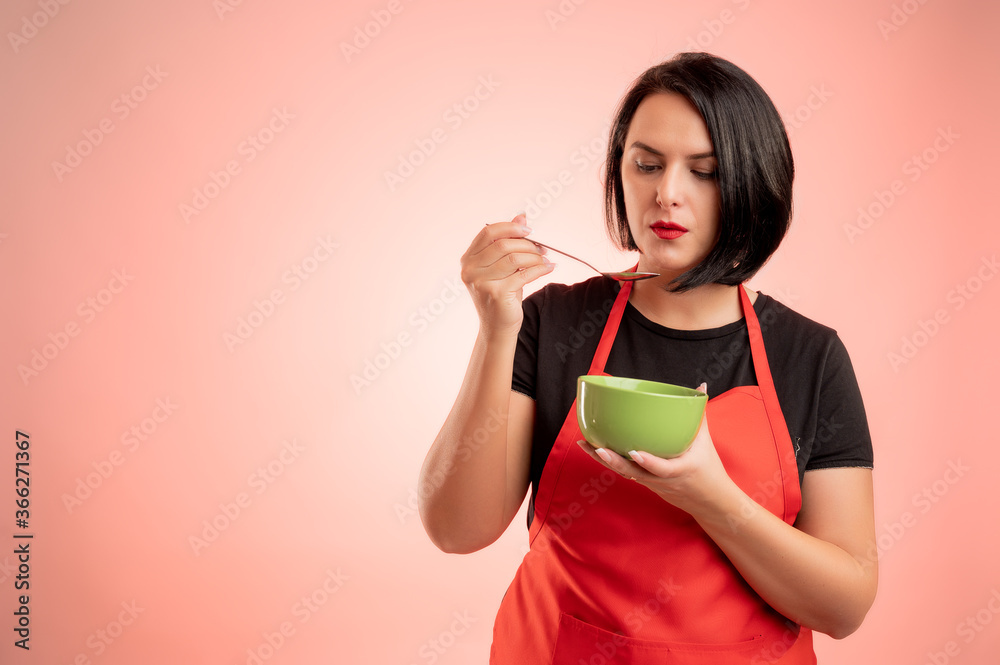 Woman employed at supermarket with red apron and black t-shirt cool the soup, hold the bowl in her hand Woman employed at supermarket with red apron and black t-shirt cool the soup, hold the bowl in her hand
