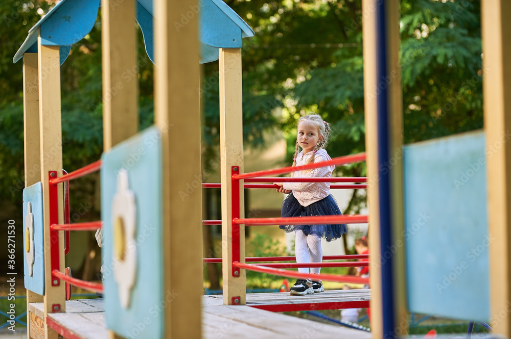 a little girl with blond hair plays on the playground and climbs on the game slides and steps of the house