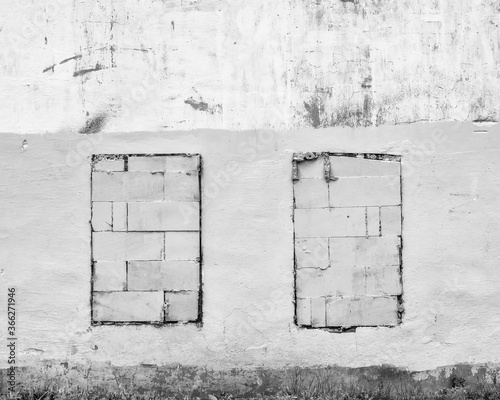 Old abandoned crumbling plaster  facade building wall  with walled windows black and white