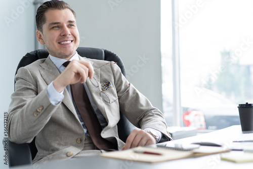 Male casual office worker smiling in office, sitting at workplace