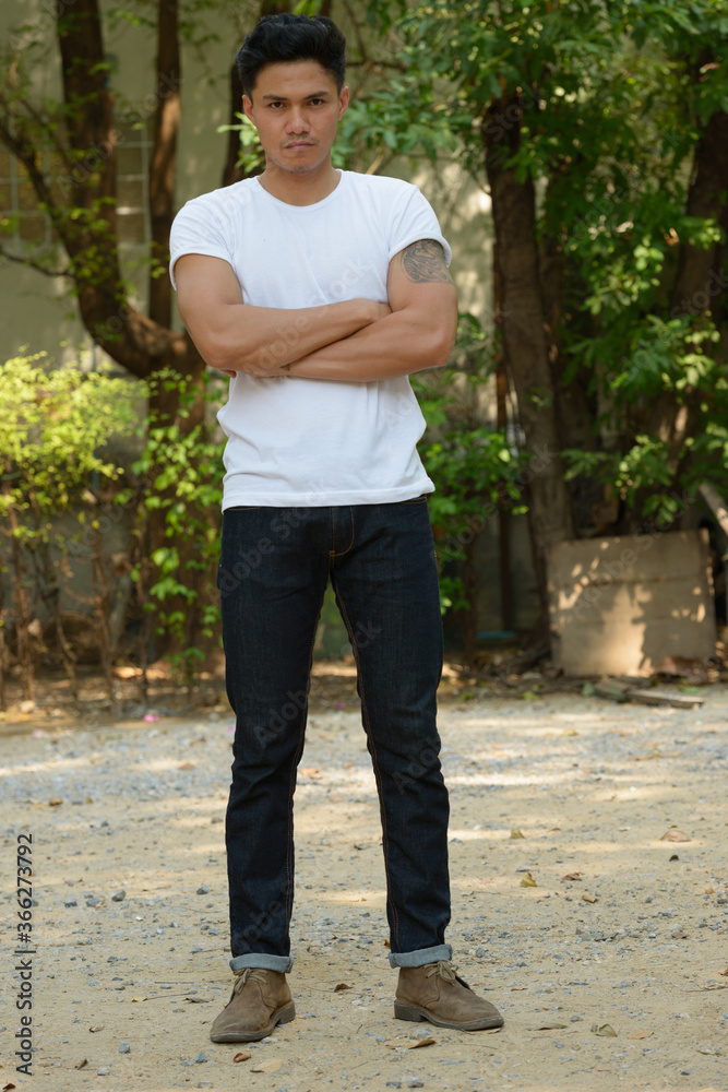 Full body shot of handsome Asian man with arms crossed at the park outdoors Full body shot of handsome Asian man with arms crossed at the park outdoors