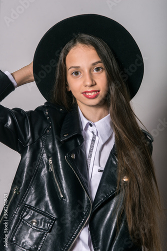 A teenage girl in a trendy leather jacket and an even hat on a white background. Teenage fashion. Street fashion. Beauty and fashion