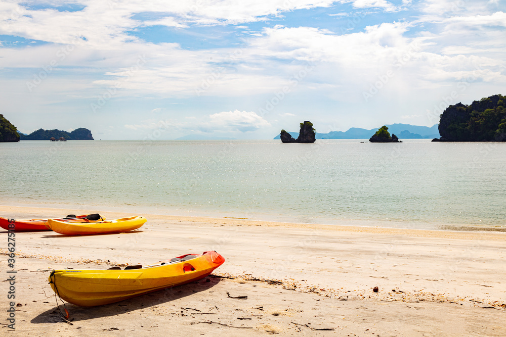 Two yellow kayak boats lie on the sandy beach of Tanjung Rhu Beach in Langkawi, Malaysia. Idyllic view over the beach. White clouds on blue sky. In the background the rocks in the water off the coast Two yellow kayak boats lie on the sandy beach of Tanjung Rhu Beach in Langkawi, Malaysia. Idyllic view over the beach. White clouds on blue sky. In the background the rocks in the water off the coast