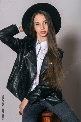 A teenage girl in a trendy leather jacket and an even hat on a white background. Teenage fashion. Street fashion. Beauty and fashion