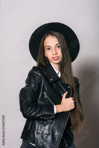 A teenage girl in a trendy leather jacket and an even hat on a white background. Teenage fashion. Street fashion. Beauty and fashion