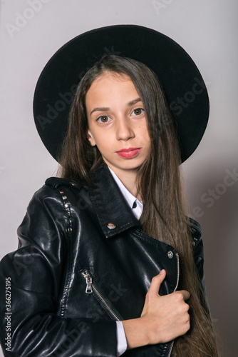 A teenage girl in a trendy leather jacket and an even hat on a white background. Teenage fashion. Street fashion. Beauty and fashion