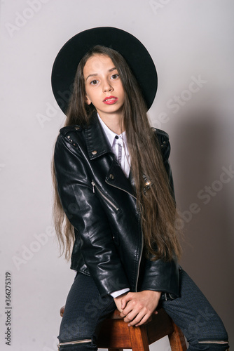 A teenage girl in a trendy leather jacket and an even hat on a white background. Teenage fashion. Street fashion. Beauty and fashion