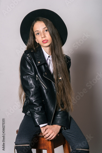 A teenage girl in a trendy leather jacket and an even hat on a white background. Teenage fashion. Street fashion. Beauty and fashion