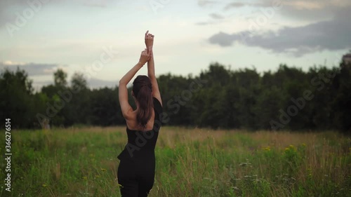 Back view of a young happy woman is raising arms in nature. Smiling girl outdoor relaxing. 