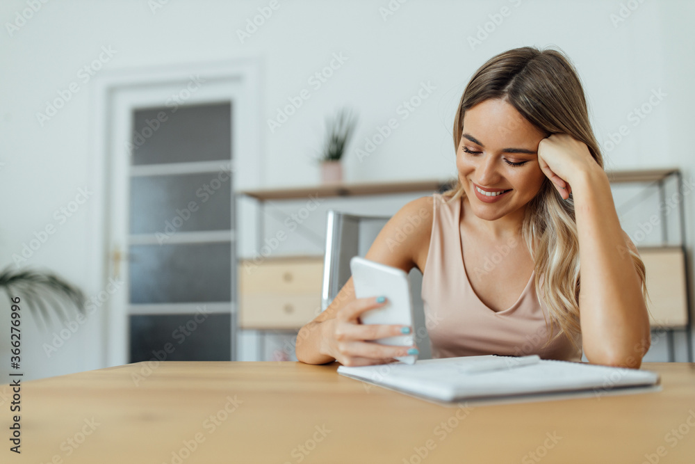 Close-up portrait of a cheerful college student using smart phone while studying at home. Close-up portrait of a cheerful college student using smart phone while studying at home.