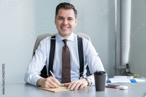 Smiling young businessman sit at desk talk on webcam having video call or conversation with client, motivated male coach or trainer speak shoot online tutorial, record training course