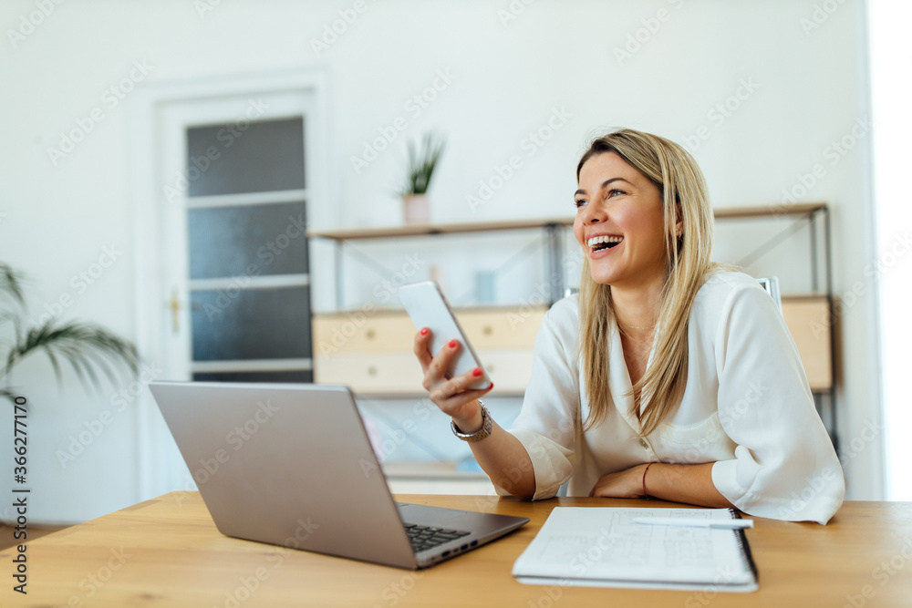 Portrait of a businesswoman holding smart phone and laughing at workplace. Portrait of a businesswoman holding smart phone and laughing at workplace.
