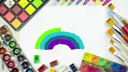 rainbow drawing animation on a flat lay painting background with white paper sheet, palette of watercolor paints, brushes, colorful chalk crayons, children's backdrop top view