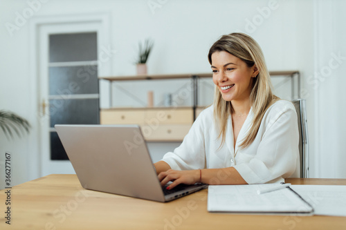 Beautiful smiling woman using laptop computer in home office, portrait.