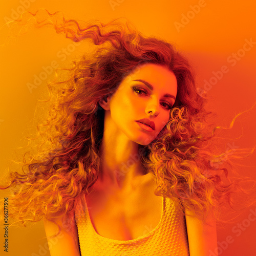 High Fashion. Woman in colorful neon gold light, make-up. Sexy blond girl, stylish curly hair, trendy makeup. Golden neon portrait. Creative beauty, fashionable model face, voluminous hairstyle