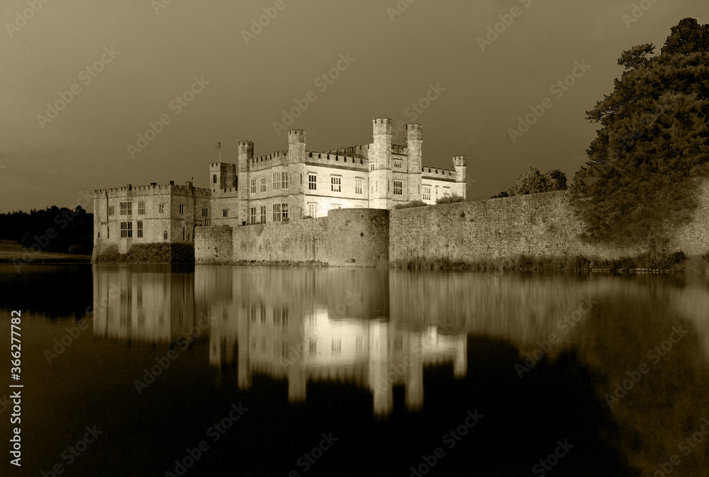 Famous illuminated Leeds Castle In the United Kingdom mirrored in surrounding Water early in the evening. Sepia colored