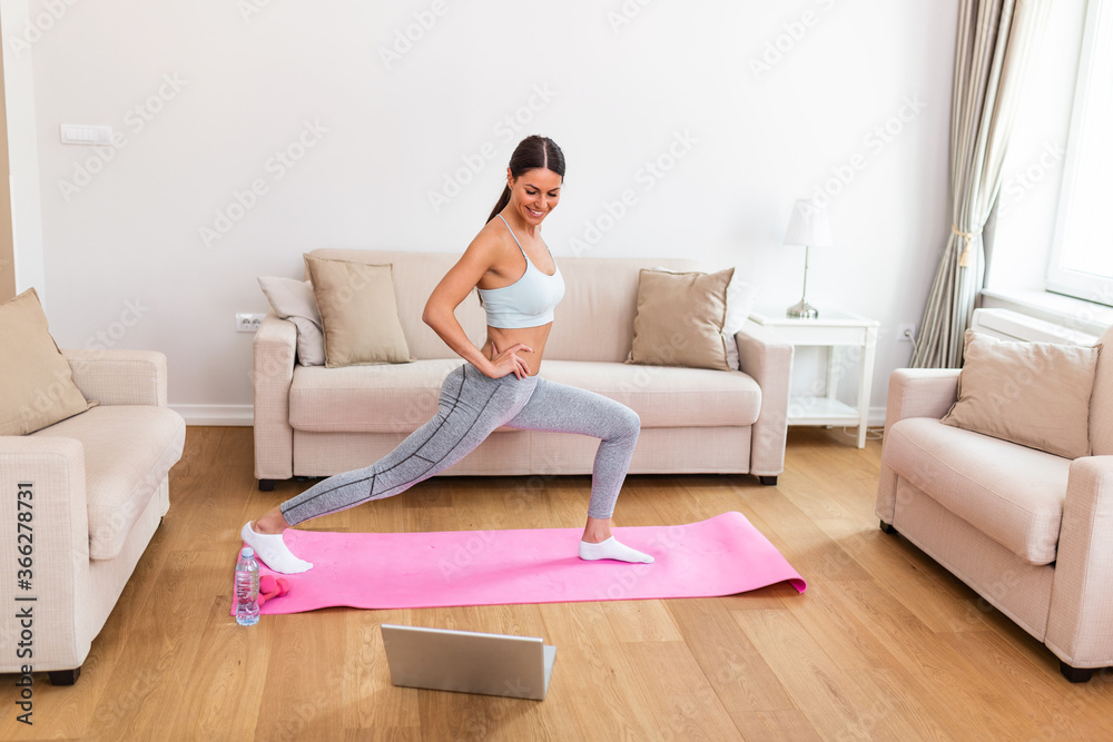Gorgeous young woman on exercise mat at home and watching workout tutorial online on laptop. Video lesson. Young woman repeating exercises while watching online workout session Gorgeous young woman on exercise mat at home and watching workout tutorial online on laptop. Video lesson. Young woman repeating exercises while watching online workout session