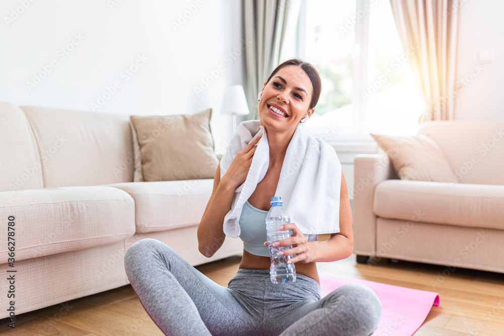 Beautiful young woman wiping sweat with a towel, exhausted after the daily training and drinking water from the bottle Beautiful young woman wiping sweat with a towel, exhausted after the daily training and drinking water from the bottle