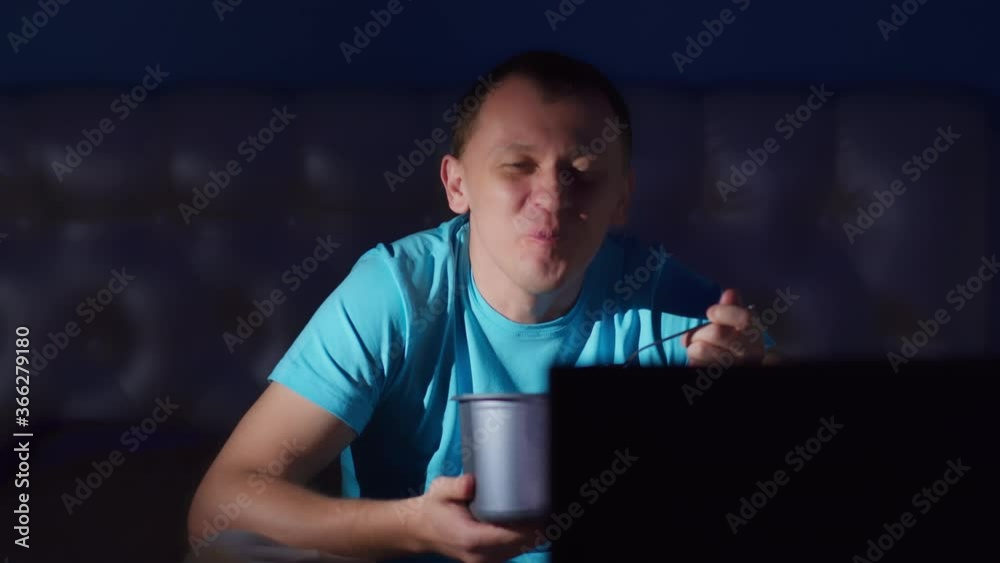 Man watches TV at night eating ice cream and smile, close-up, camera movement Man watches TV at night eating ice cream and smile, close-up, camera movement