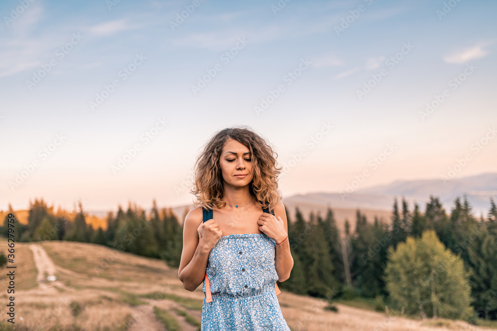 Curly young woman with a bunch of chamomiles enjoying the view in the top of mountain on a hot summer day. Lifestyle concept Curly young woman with a bunch of chamomiles enjoying the view in the top of mountain on a hot summer day. Lifestyle concept