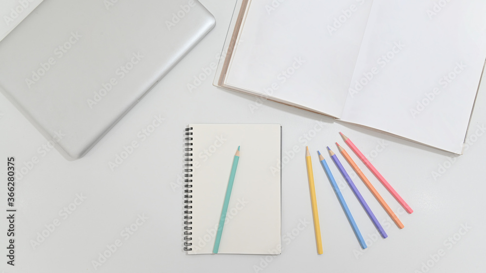 Top view of modern workspace desk with laptop, blank notebook and crayon on white table. concept work from home. Top view of modern workspace desk with laptop, blank notebook and crayon on white table. concept work from home.