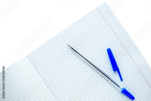 Ballpoint pen with a blue cap on the school notebook in a cage on a white background.