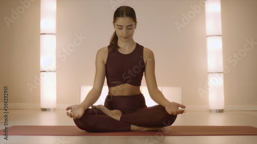 Woman sitting in lotus pose on mat indoors. Trainer practicing yoga in studio