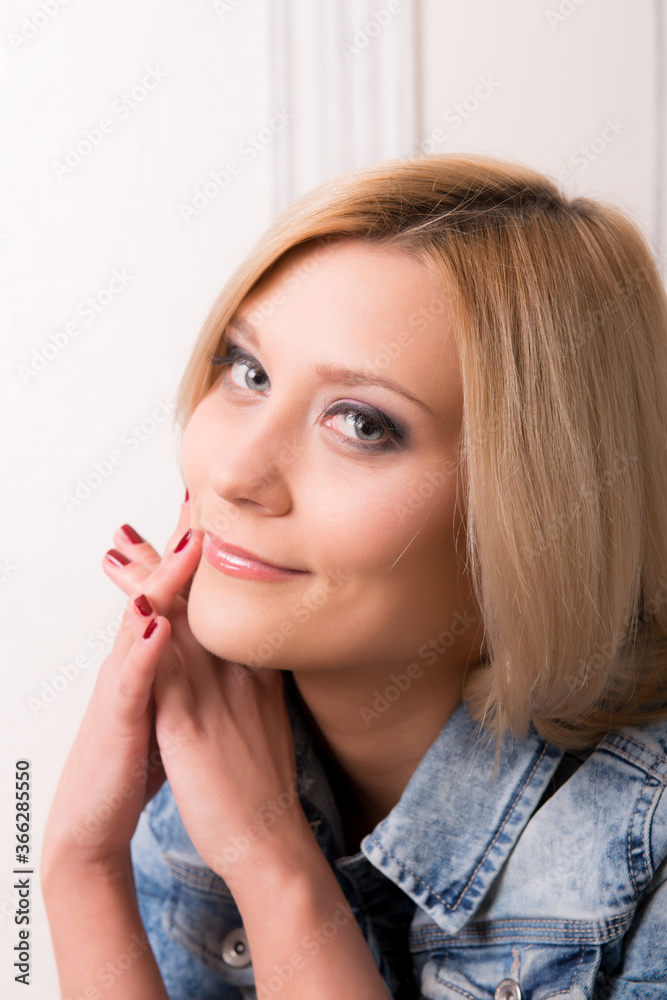 Stylish blonde girl rests her hands on her chin and smiles on a light background close-up. Stylish blonde girl rests her hands on her chin and smiles on a light background close-up.