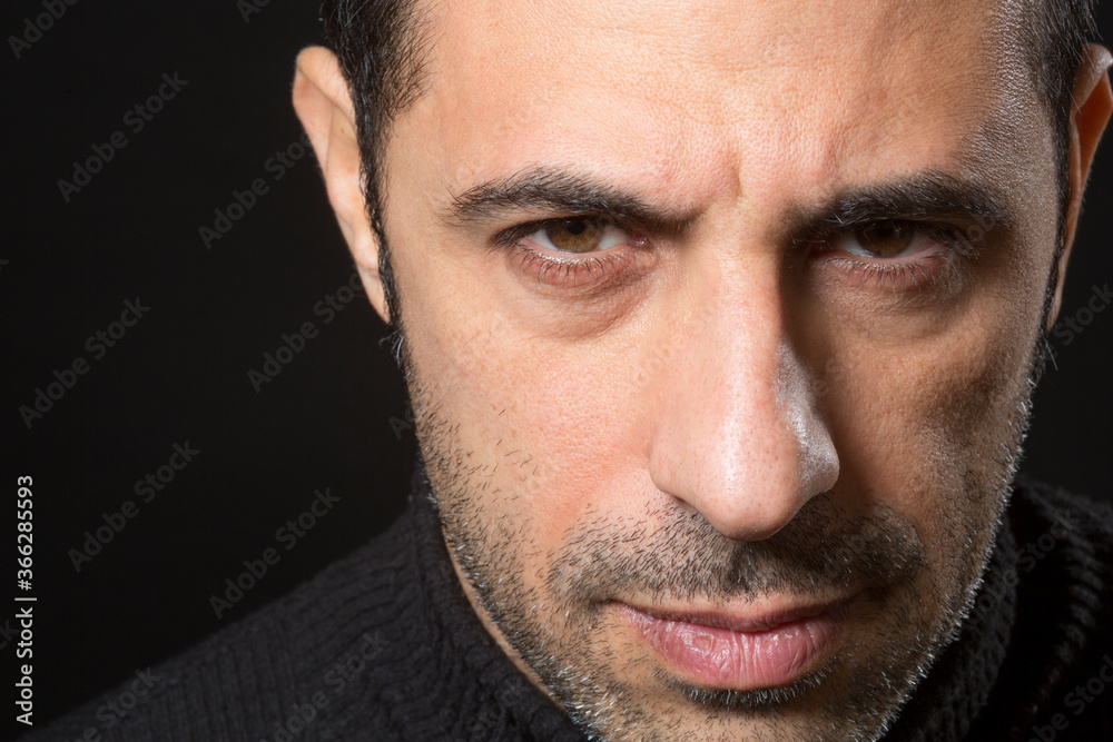 Fototapeta premium Ritratto stretto di un uomo che guarda con espressione dura e severa isolato nell'oscurità