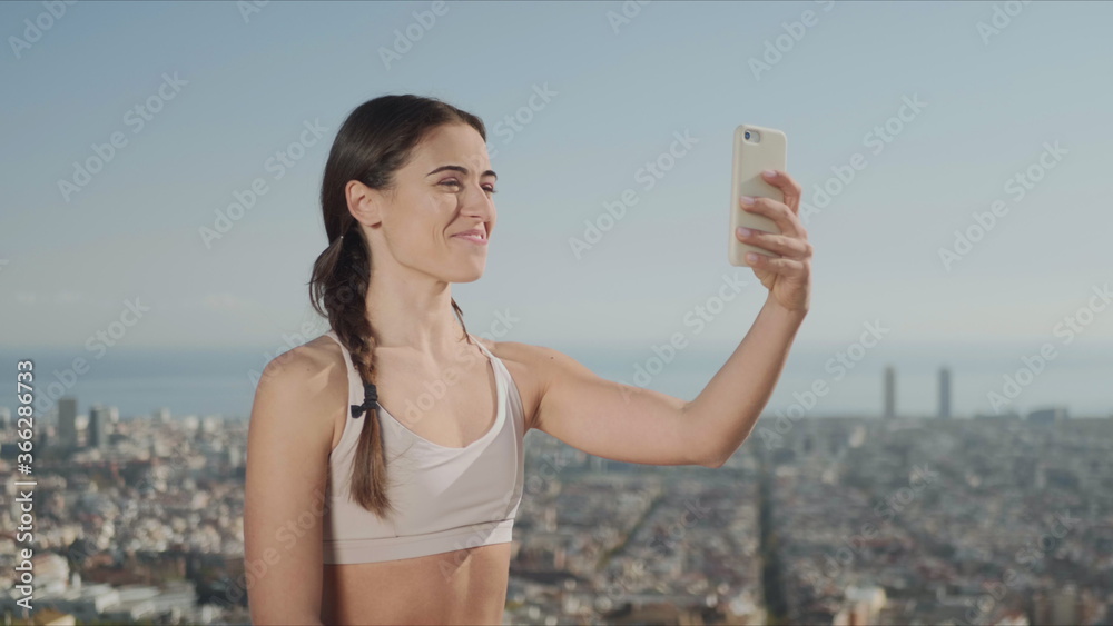 Sportswoman talking with friend online by video call against city of Barcelona Sportswoman talking with friend online by video call against city of Barcelona