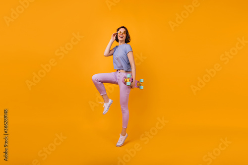 Fototapeta Naklejka Na Ścianę i Meble -  Full-length portrait of pretty short-haired woman with longboard. Indoor shot of spectacular girl in summer outfit and yellow-colored glasses.