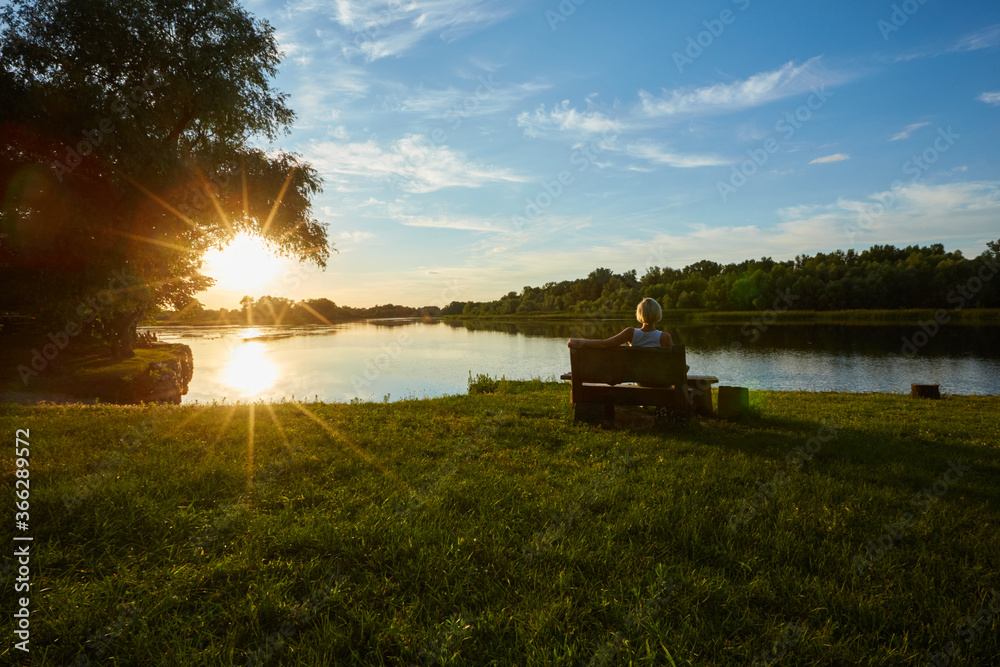 Fototapeta premium Woman Sitting On Bench During A Beautiful Sunset