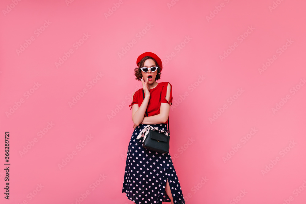 Fashionable french girl in long black skirt posing in studio. Enchanting short-haired woman in beret standing on pink background.