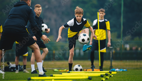 Teenage boys on football training session with two young coaches. Junior level soccer player kicking ball during practice session. Soccer training drills with hurdles agility © matimix