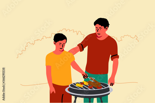 Fatherhood, childhood, holiday, education concept. Young man dad teaching child kid son how to grill standing together in backyard. Family gathering and spending time on summer vacation or fathers day