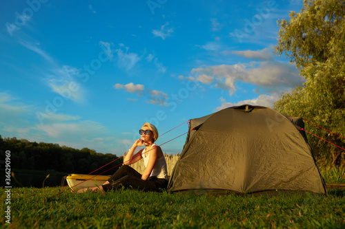 Travel, kayaking and hiking concept. Portrait of young beautiful woman sitting near green tent with kayak near river.