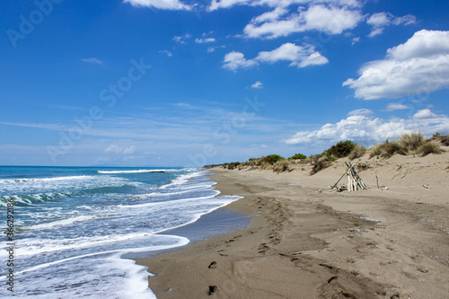 Collelungo beach, Alberese, Tuscany, Italy. Rough sea with white foam that reaches the dunes. On the sand there are footprints and a hut made of logs.