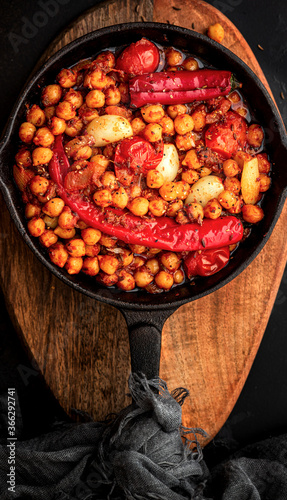 Spicy chickpeas with hot red peppers, tomatoes, cumin, garlic and other spices in a frying pan on a black background top view. Chickpeas stewed with vegetables and spices, oriental cuisine. 