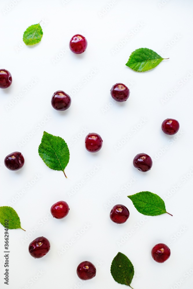 Bright red juicy ripe cherry with green leaves scattered on a white background. Bright red juicy ripe cherry with green leaves scattered on a white background.