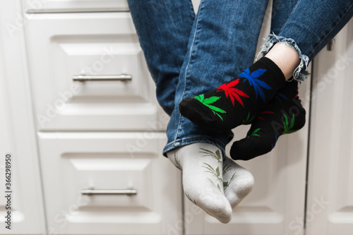 Lovers sit in the kitchen and touch their feet. A guy with a girl. The legs are wearing jeans and socks with the image of marijuana. Added noise. Close-up.
