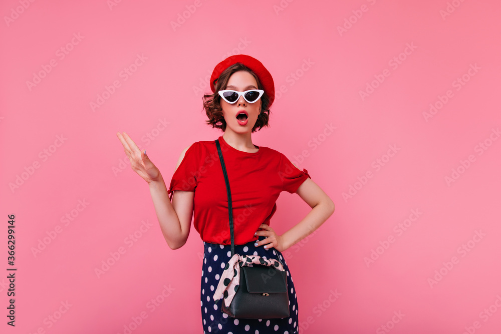 Glamorous french woman in red t-shirt posing in studio. Indoor photo of brunette european girl in beret and sunglasses. Glamorous french woman in red t-shirt posing in studio. Indoor photo of brunette european girl in beret and sunglasses.