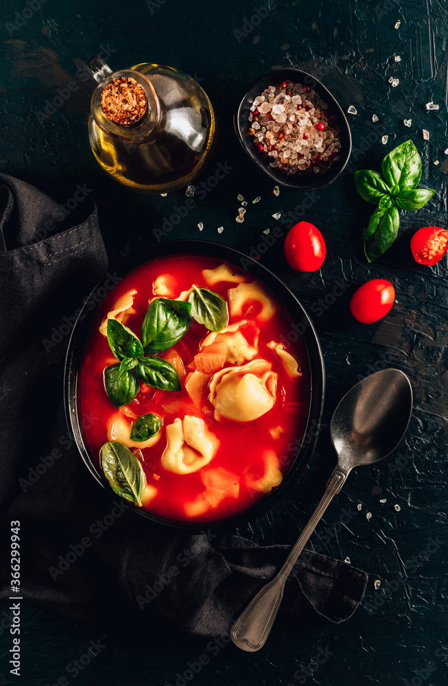 Tomato soup with tortellini in black bowl on dark background. Tomato soup with tortellini in black bowl on dark background.
