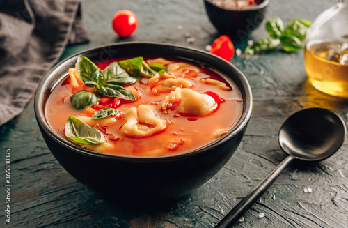 Fényképezés Tomato soup with tortellini in black bowl on dark background.