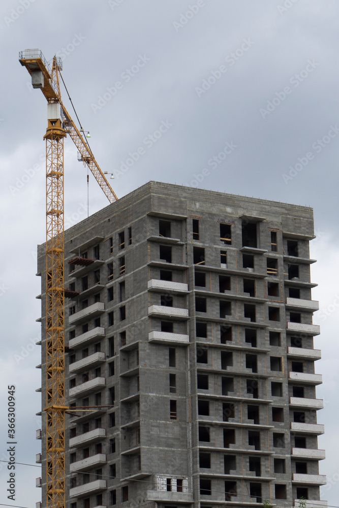 Unfinished multi-storey building. Construction crane on a background of gloomy sky.