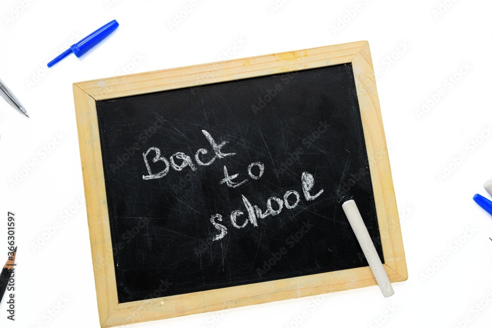 Fototapeta premium A black school board with chalk inscription back to school with pens and pencils on a white background.