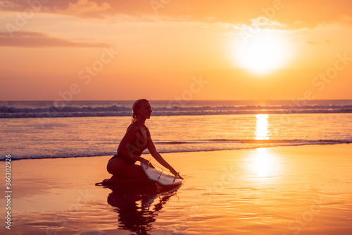 Portrait of surfer girl with beautiful body on the beach with surfboard at colourful sunset time..