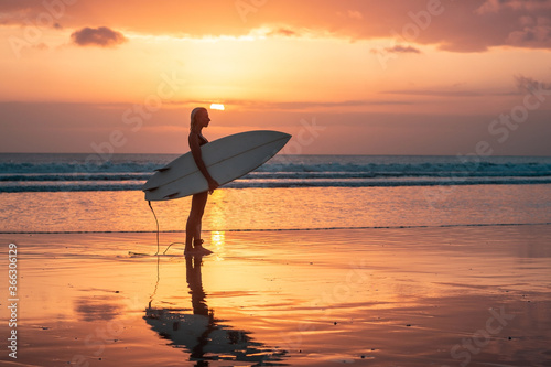 Portrait of surfer girl with beautiful body on the beach with surfboard at colourful sunset time.