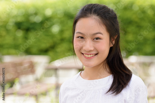 Face of happy young beautiful Asian woman smiling at the coffee shop outdoors