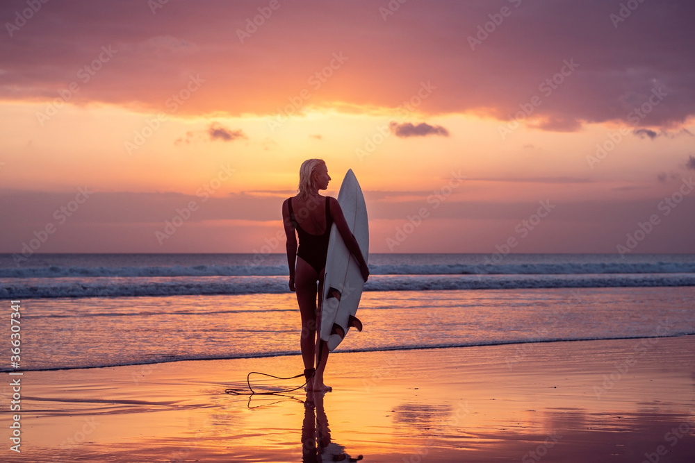 Portrait of surfer girl with beautiful body on the beach with surfboard at colourful sunset time.